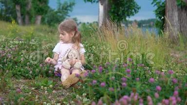 一个小女孩和一只玩具兔子在草地上的四叶草中玩耍